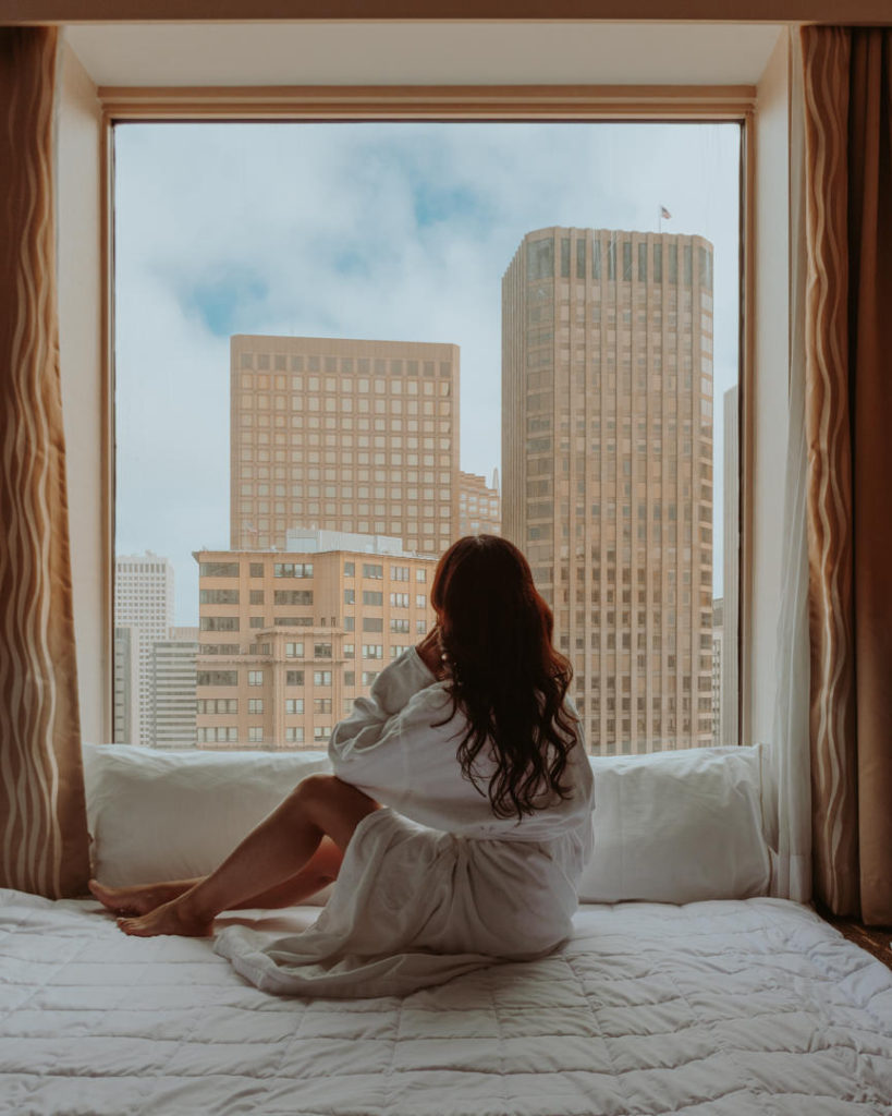 Woman in bathrobe looking out floor to ceiling window