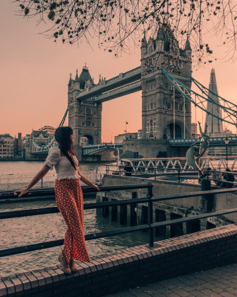 Woman standing in front of bridge at sunset