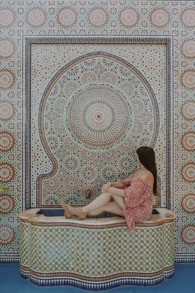 Woman in pink dress sitting on side of tiled fountain