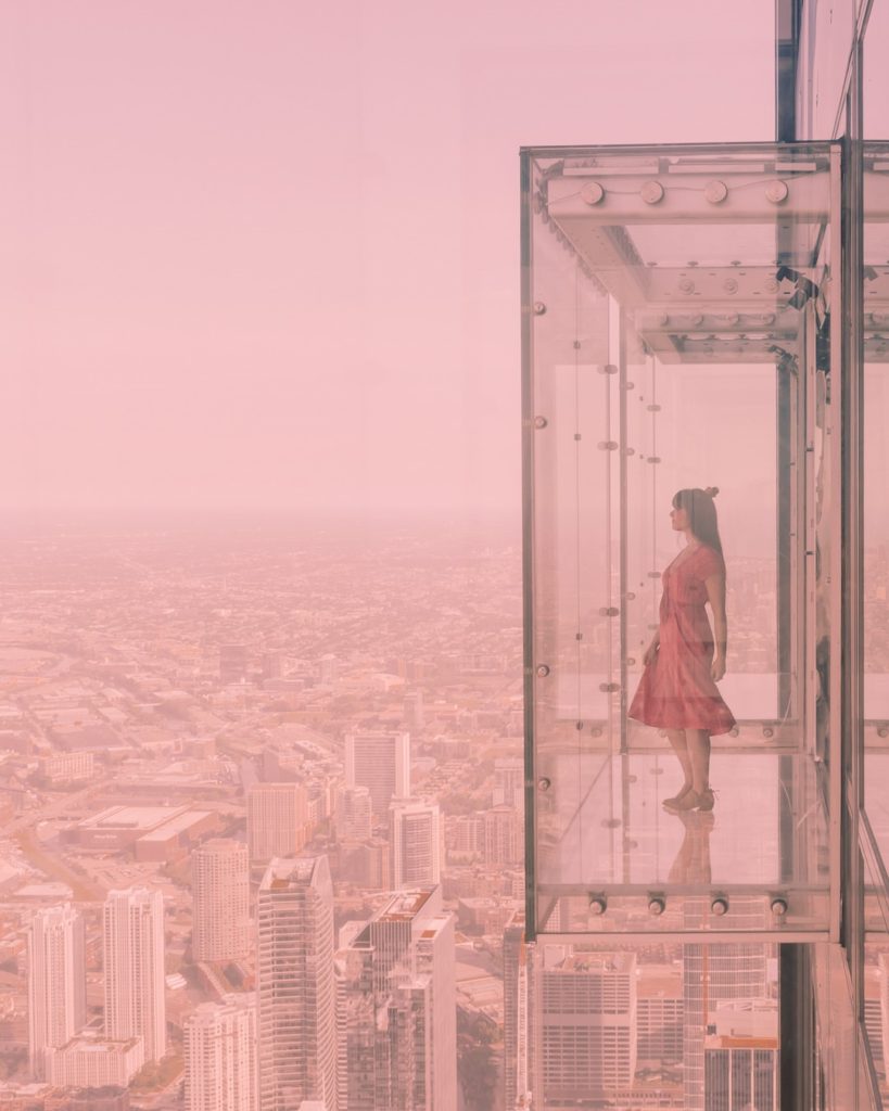 Woman in red dress standing in glass box viewing platform above city