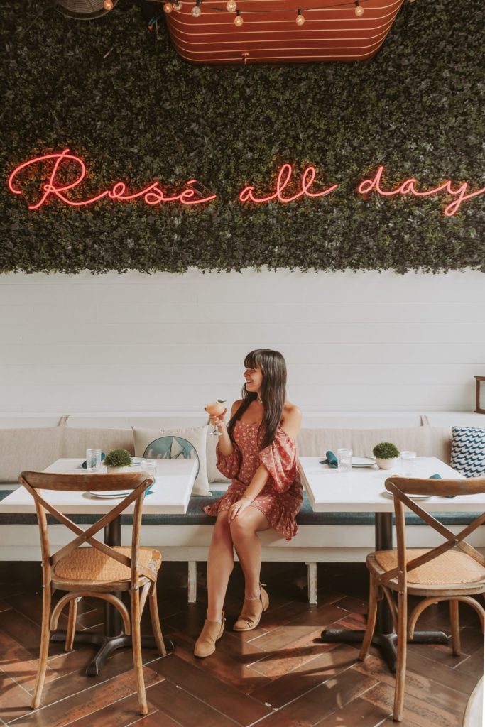 Woman in pink dress sitting in cafe under pink neon sign