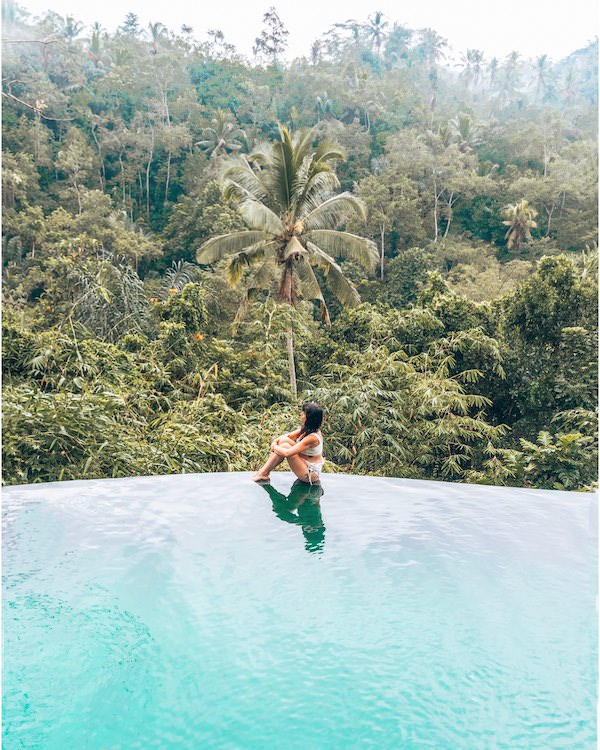 Woman sitting on edge of pool that overlooks jungle