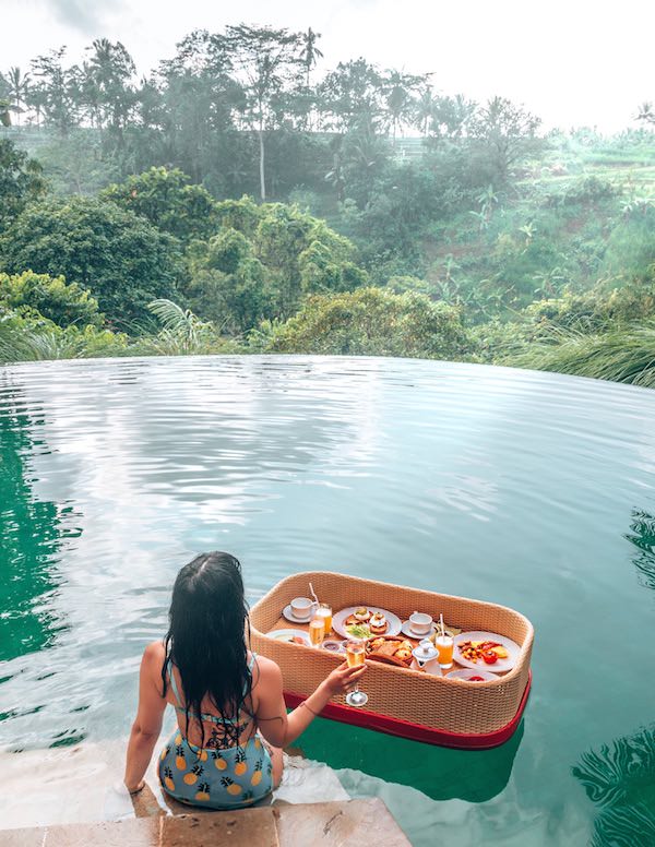 Woman sitting by pool with  breakfast on a floating Balinese tray