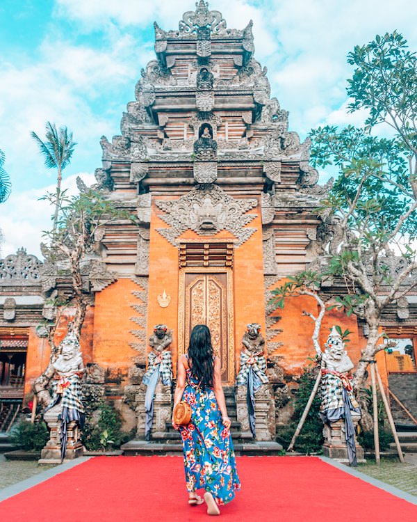 Woman in blue dress standing in front of orange Balinese temple