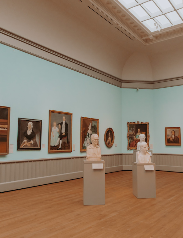 Room in art museum with light blue walls and hanging paintings
