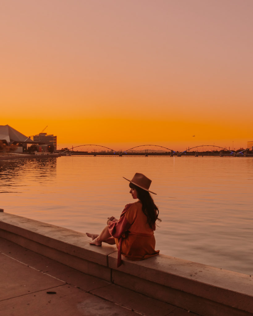 Woman sitting on edge of Tempe town lake at sunset 