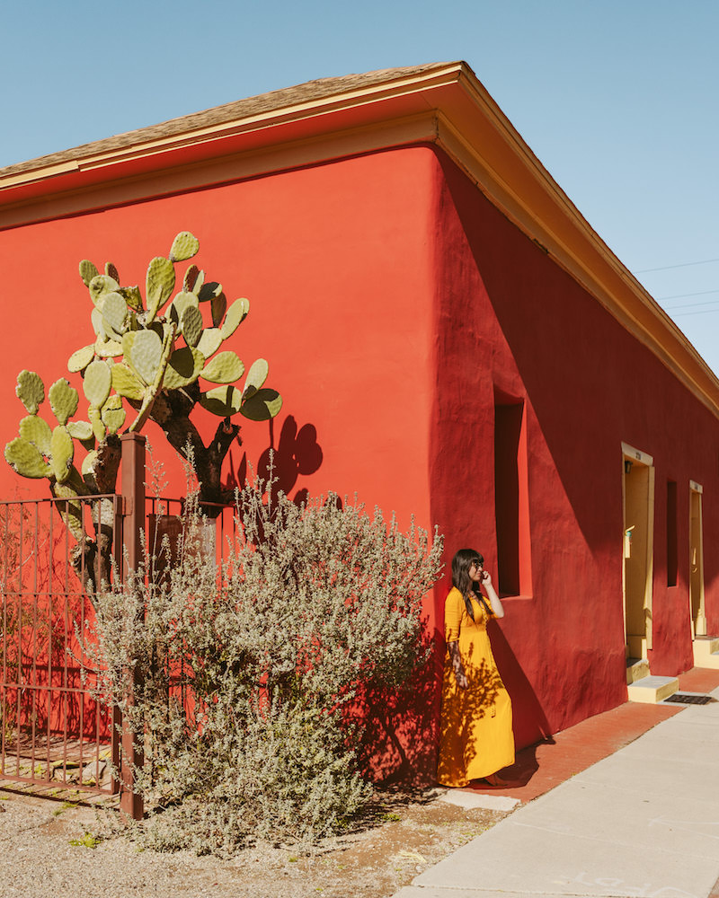 Woman in yellow dress leaning against bright rust colored building