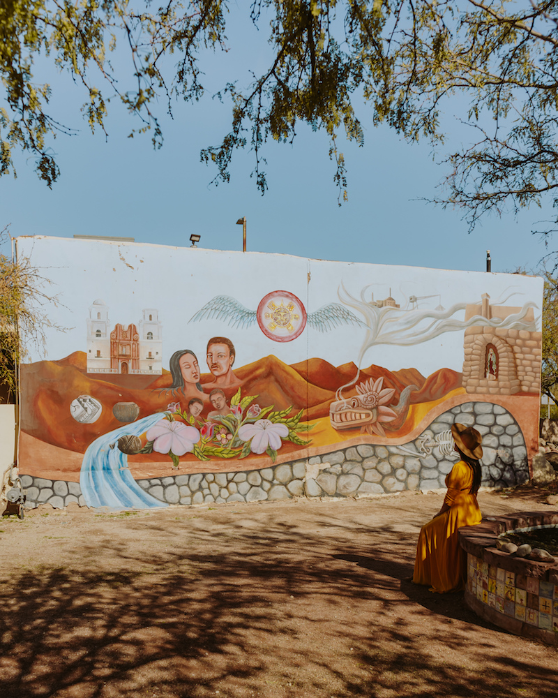 Woman in yellow dress looking at mural depicting Mexican cultural images