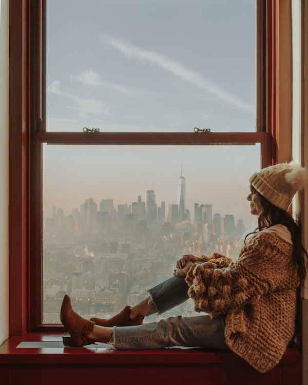 Woman sitting in windowsill looking at view of NYC skyline