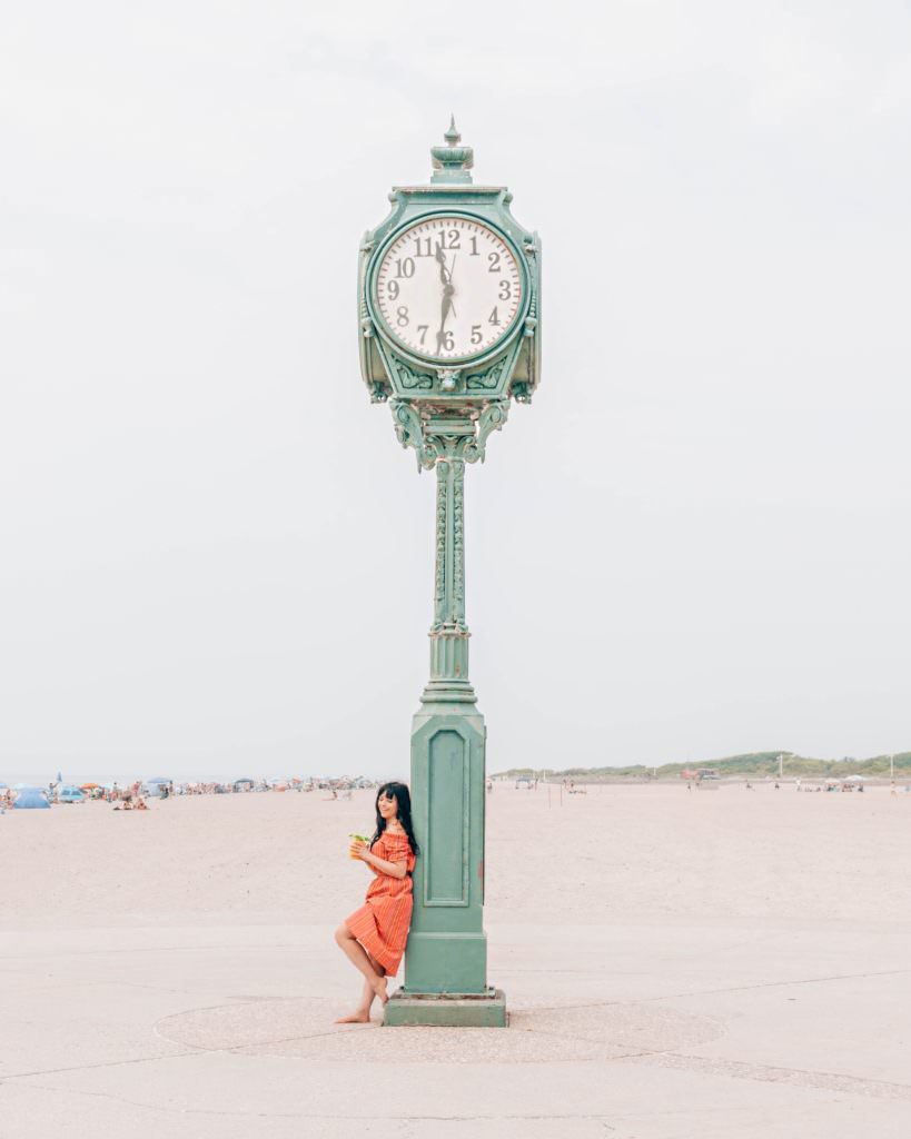 Woman standing in front of large clock at Jacob Riis beach in NYC