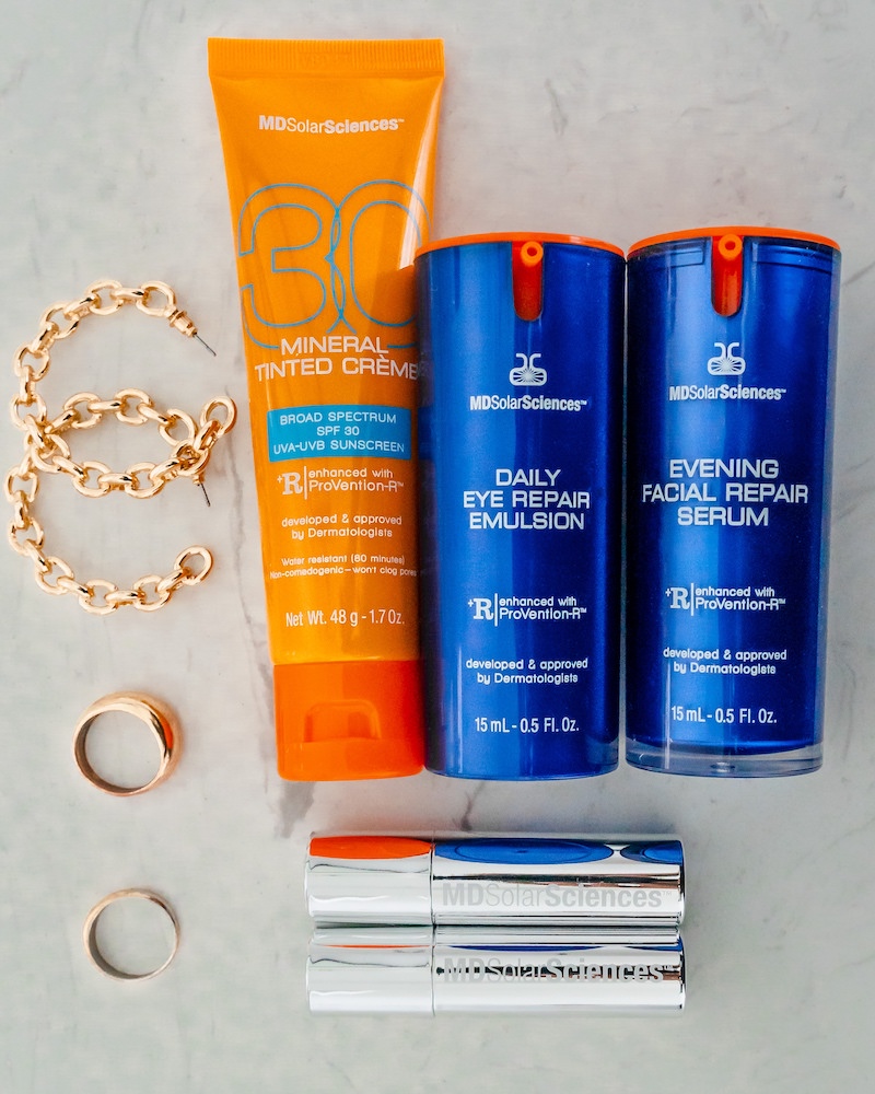 MDSolarSciences review: flatlay of Mineral Tinted Creme mineral sunscreen, Daily Eye Repair Emulsion and Evening Facial Repair Serum on marble counter with gold jewelry