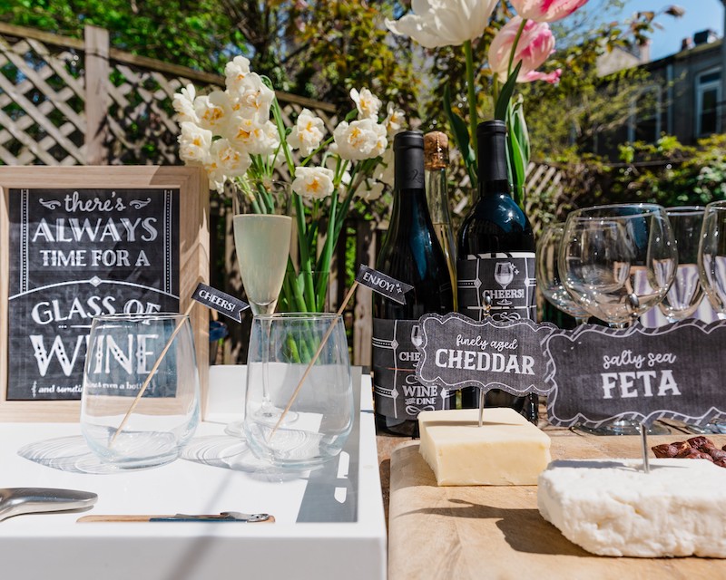 A table with flowers, wine bottles and a cheese board created using Hostess With The Mostess printables