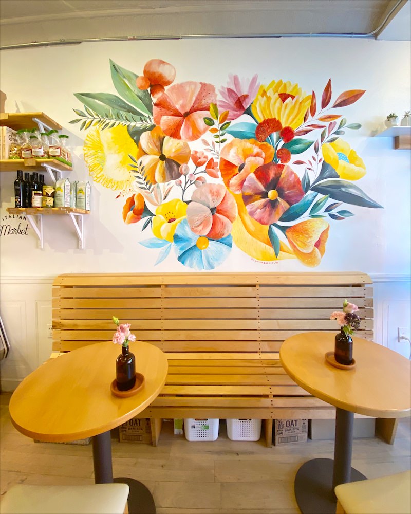 Interior of a coffee shop in Brooklyn that has wooden benches and cafe tables and a colorful floral mural.
