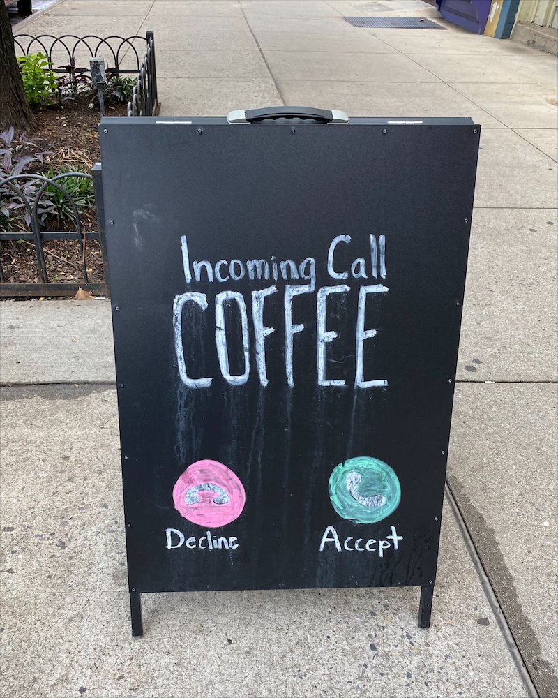 A black sign on the sidewalk that says "Incoming Call Coffee" written in chalk