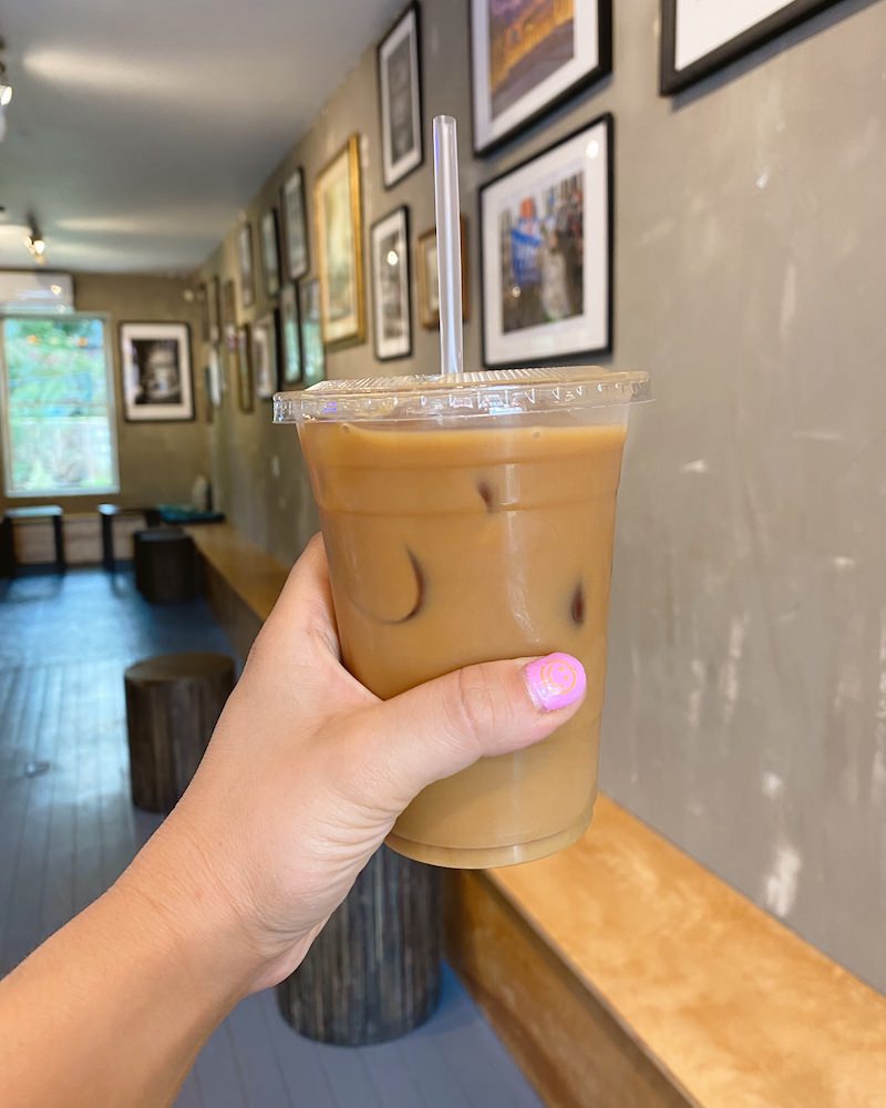A woman's hand holding an iced coffee inside a neutral themed coffee shop in Brooklyn.