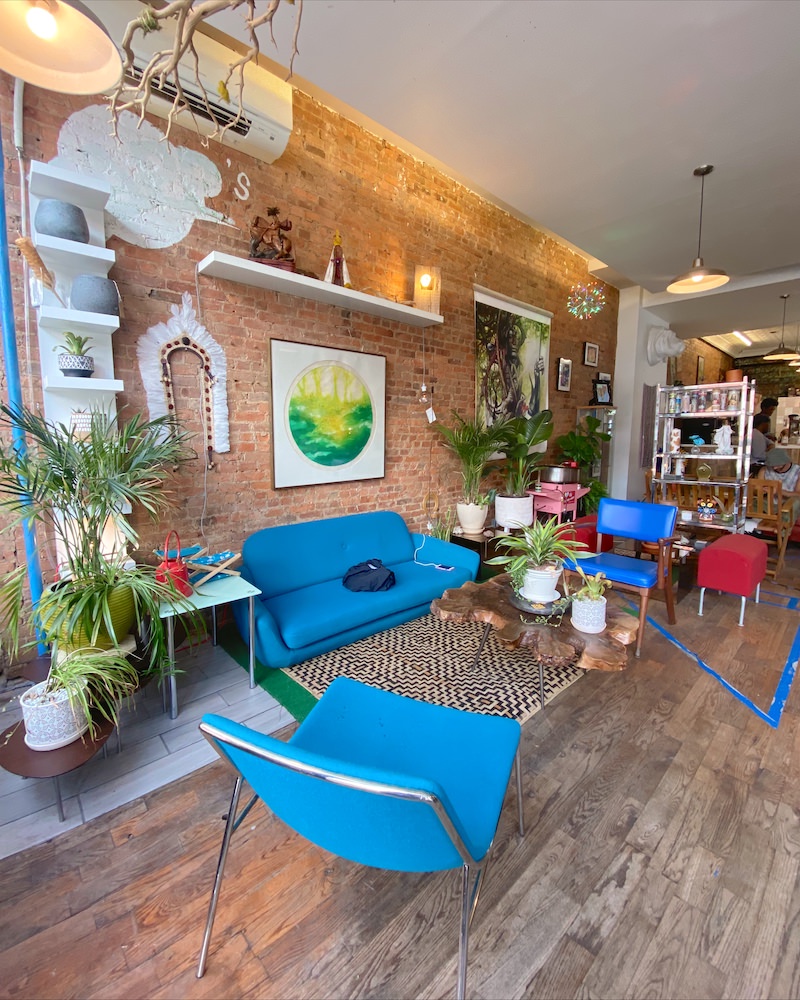 Interior of a Brooklyn coffee shop with bright blue couches, exposed red brick walls and lots of green plants.