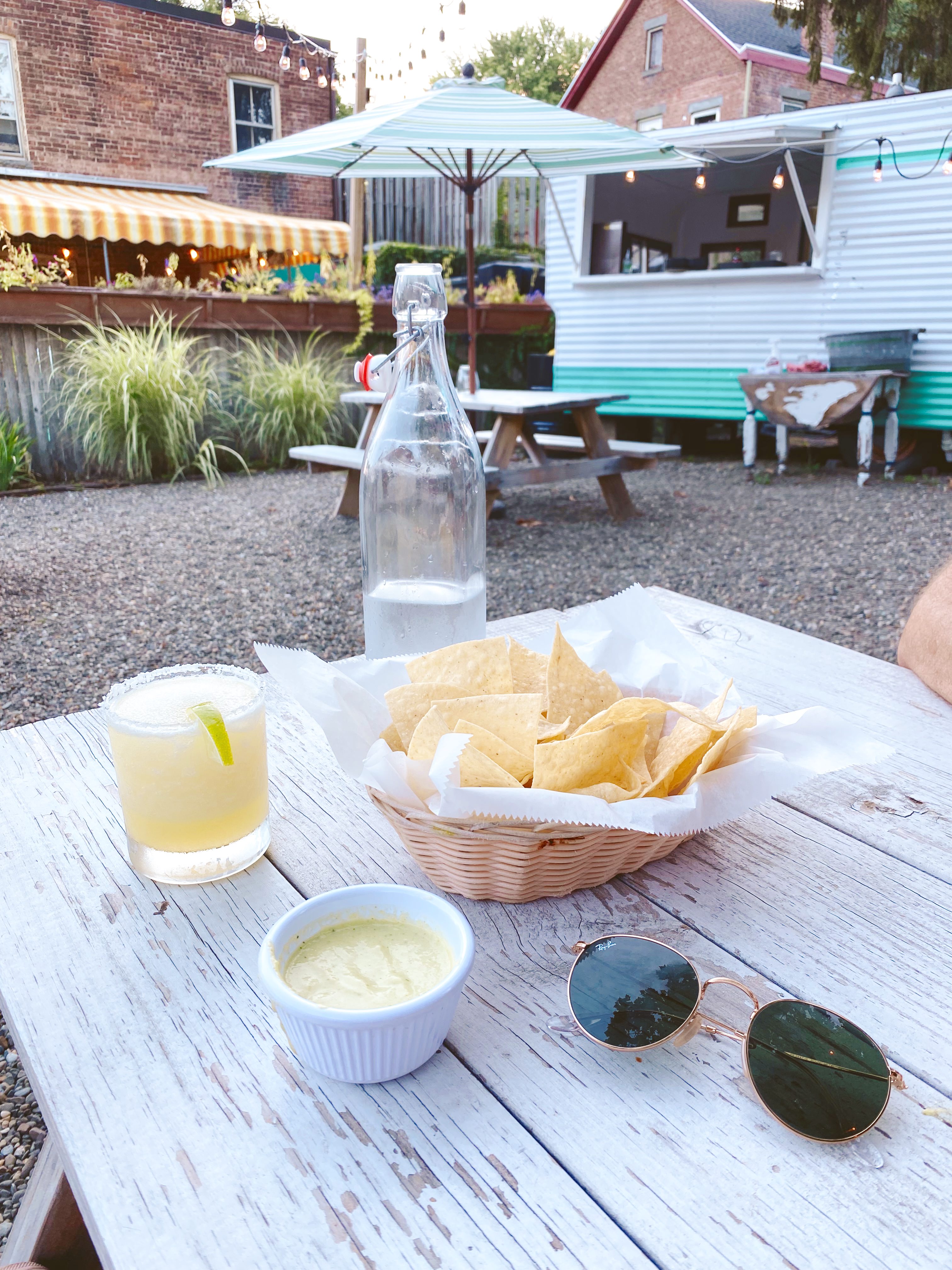 A picnic table with a basket of tortilla chips, a bottle of water, a margarita and salsa on it at Armadillo restaurant in Kingston, NY