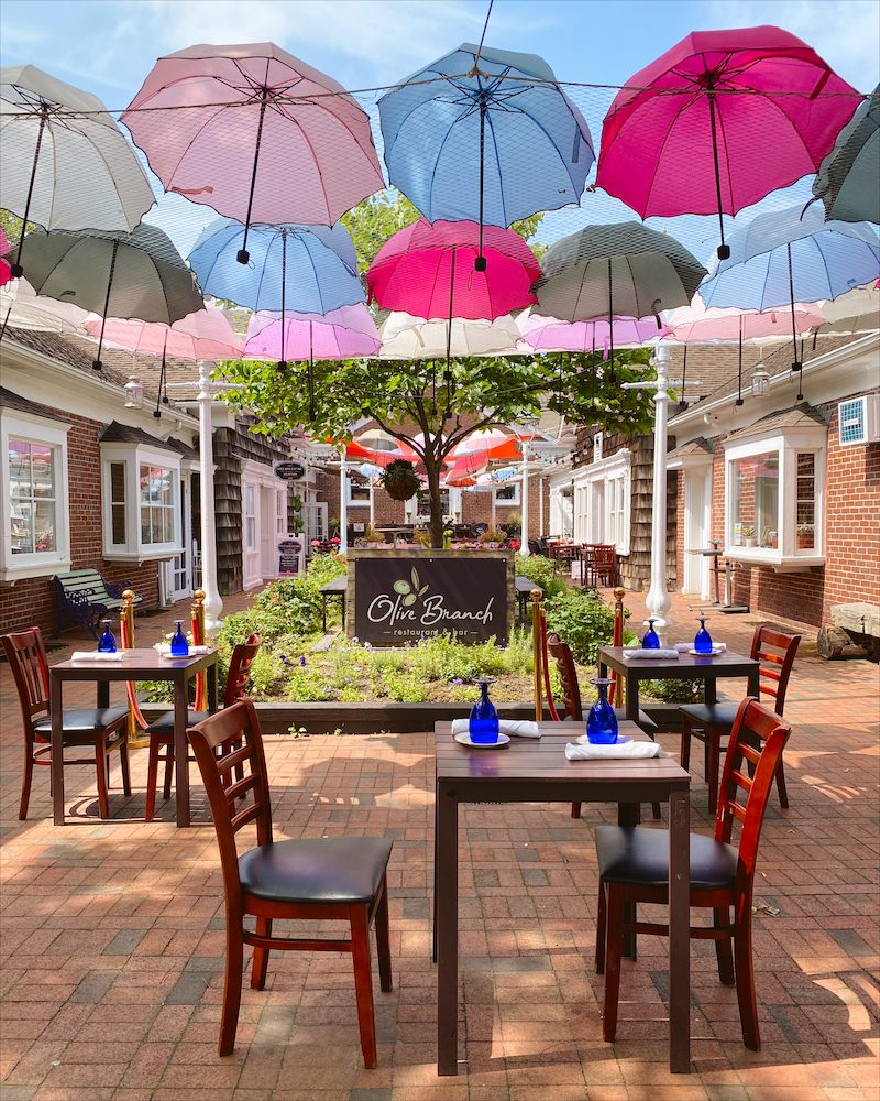 An outdoor restaurant set up with wooden tables under a canopy of brightly colored umbrellas