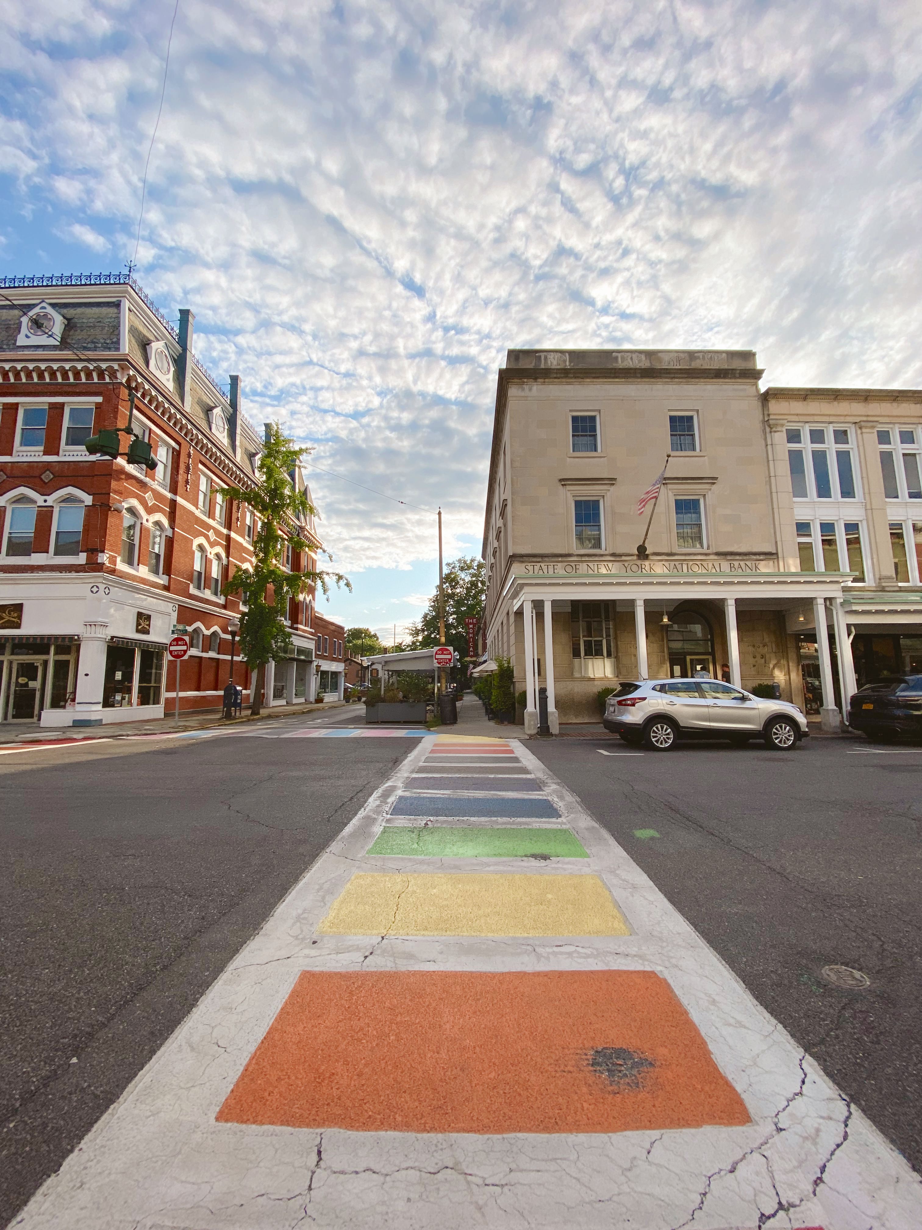 A rainbow painted crosswalk leading to the exterior of a hotel in Kingston, New York