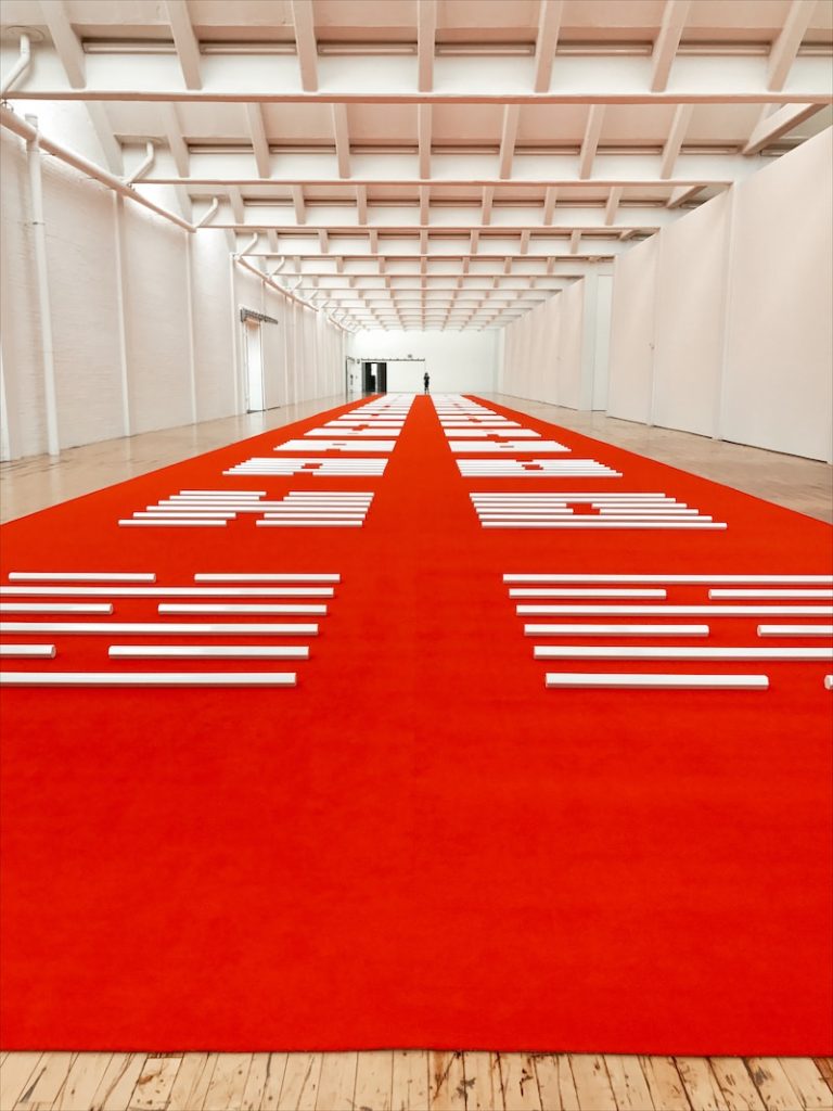 A very large white room at a museum called Dia Beacon, with a red and white floor.
