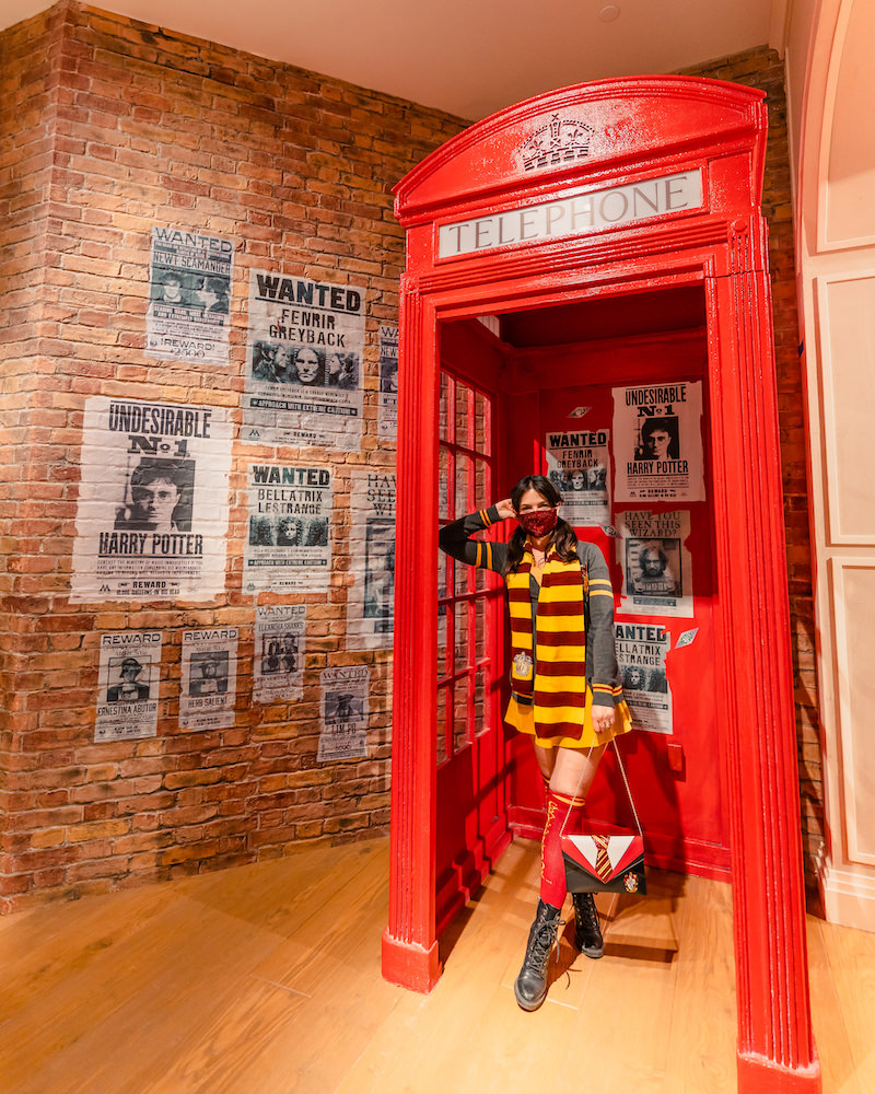 A brunette woman wearing a Harry Potter themed costume, standing in a red British style phone booth in the Harry Potter store in NYC.