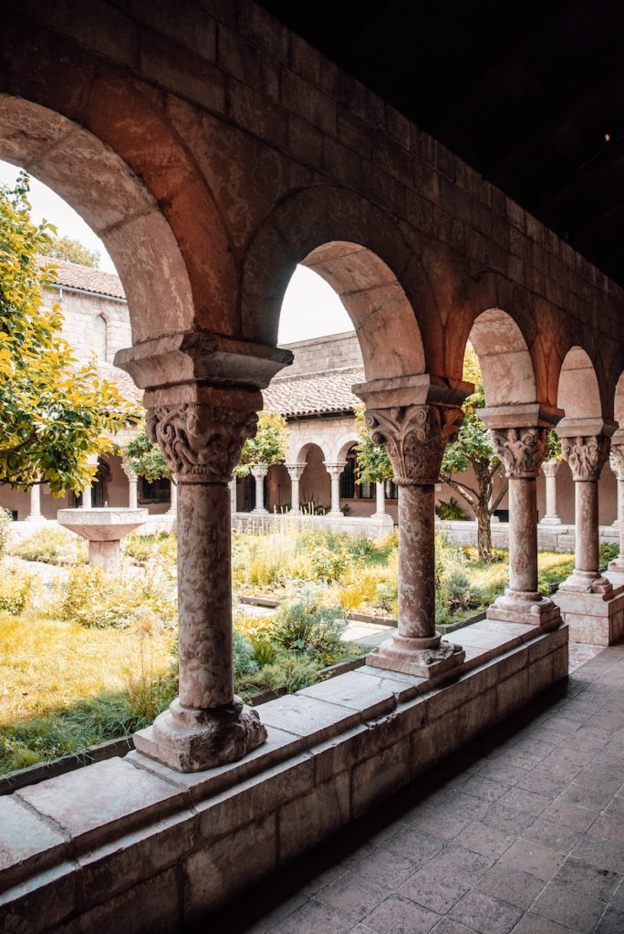 A row of medieval columns that open up to an internal courtyard garden with trees and grass at the Met Cloisters museum during fall in NYC