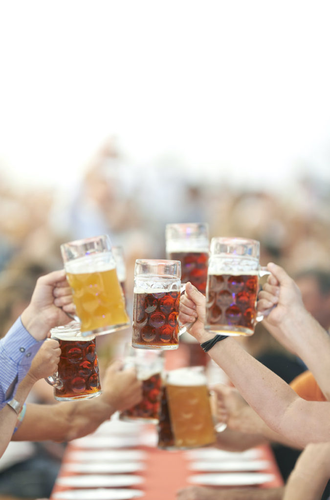 6 people's hands holding beer steins full of beer. They are clinking their glasses to cheers during fall in NYC's Oktoberfest