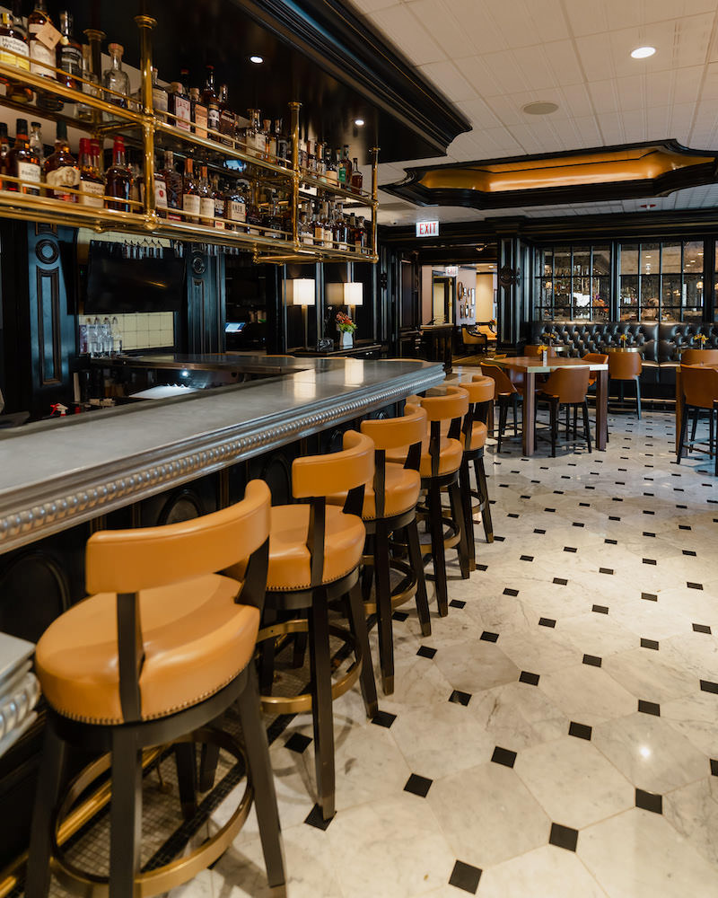 The interior of the high end restaurant Brass Tack, with black leather booth, and tan leather stools at the bar.