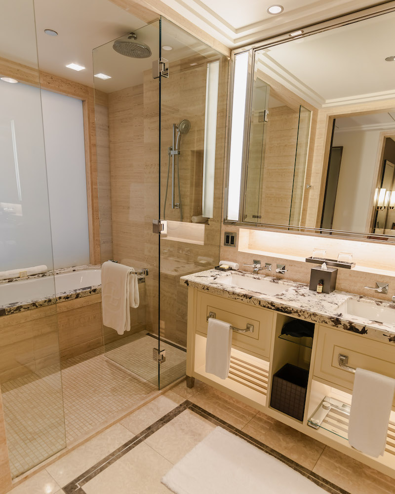 A marble bathroom hotel bathroom with dual sinks, a glassed in shower and deep bathtub. 