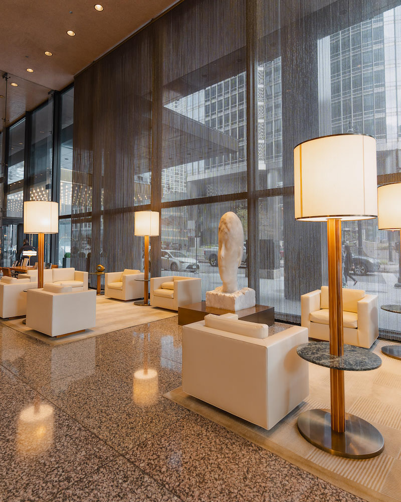 A luxury hotel lobby in Chicago with cream armchairs, large lamps and a marble statue of a person's head.