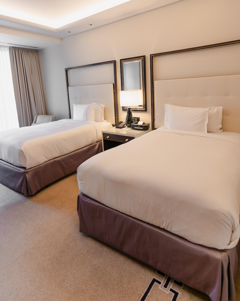 A luxury hotel room with two beds that have white sheets and brown bedskirts.