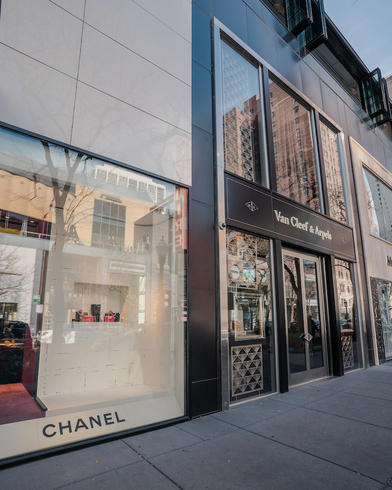 Two high-end storefronts: a beige Chanel storefront with a large window and a black and gold Van Cleef & Arpels store.