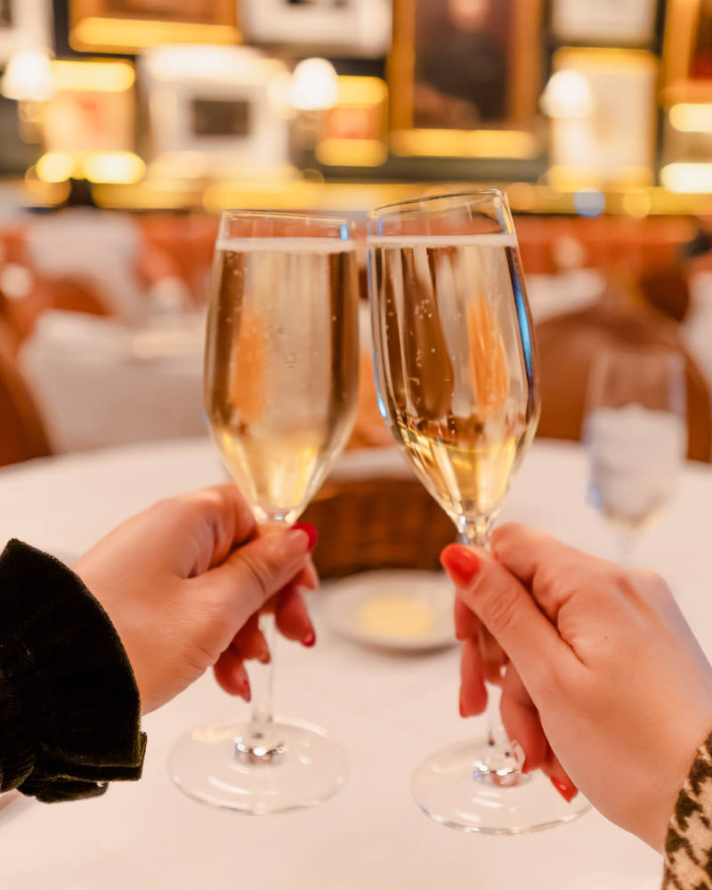 Two women's hands holding champagne glasses at a restaurant and clinking them together. 