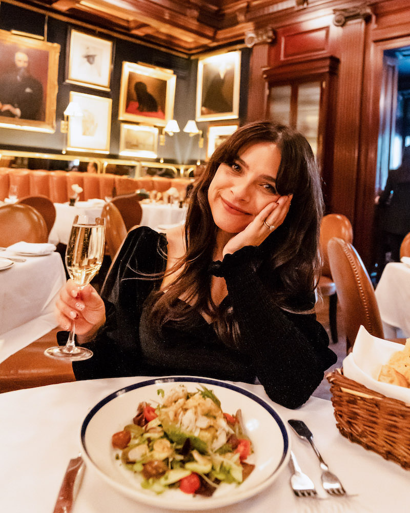 Brunette woman sitting in an elegant restaurant in Chicago. She smiling and holding a glass of champagne. 