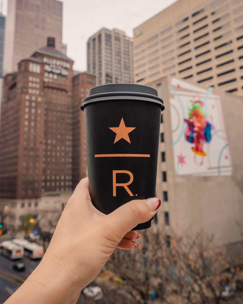 A woman's hand holding a disposible coffee cup against a Chicago city skyline view.