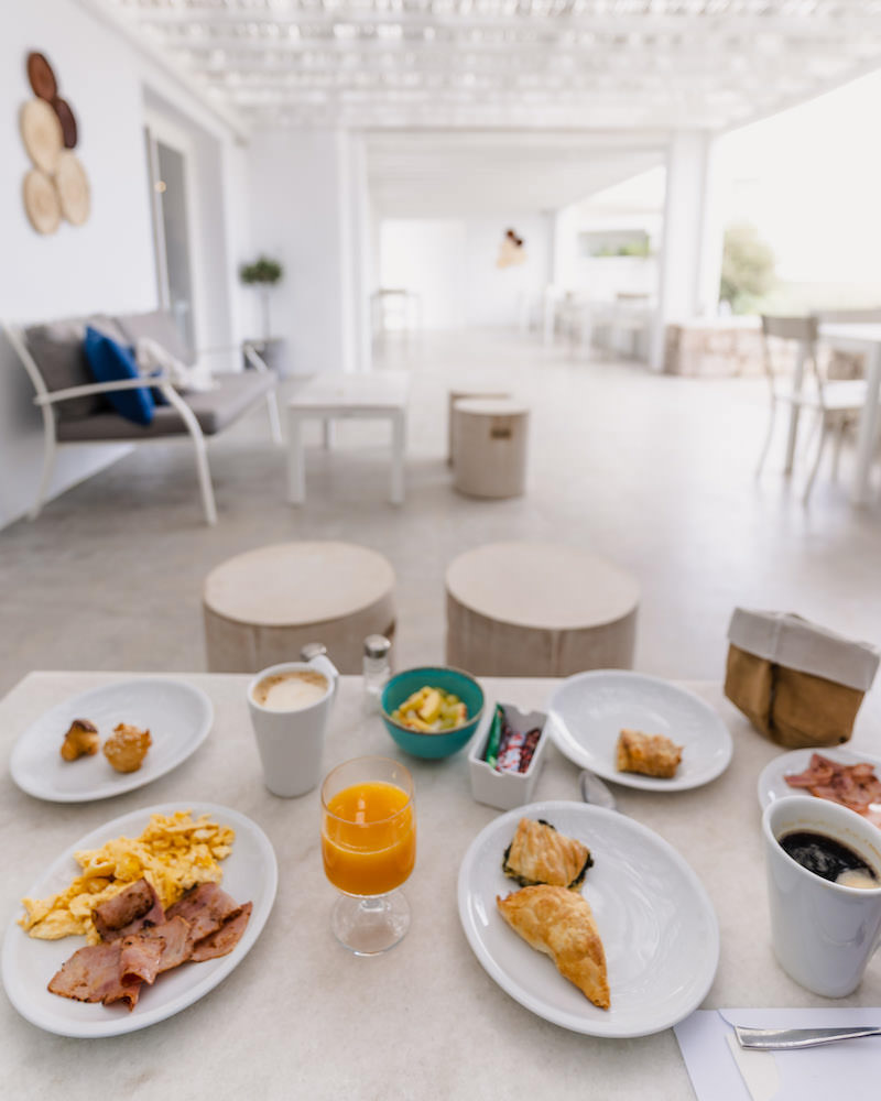 A table with an assortment of coffee, orange juice, and plates of eggs, bacon and breakfast pastries. 