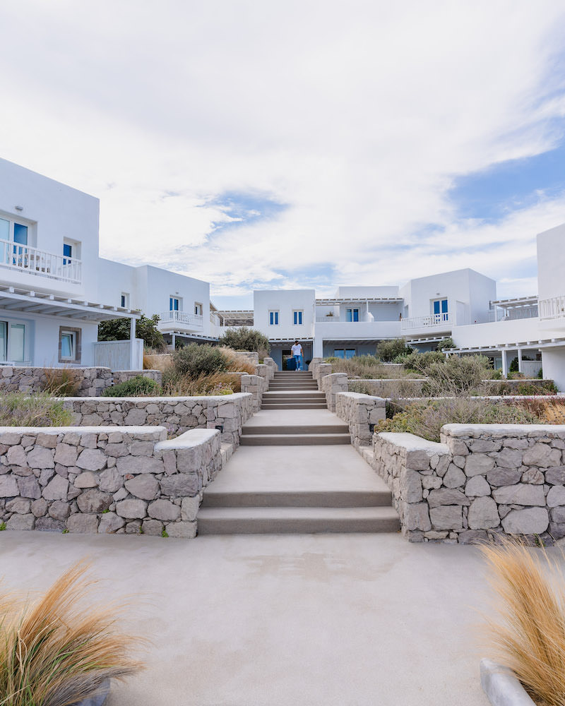 An exterior view of Milos Breeze Boutique Hotel in Greece which is a white boxy structure with blue doors and window shutters.