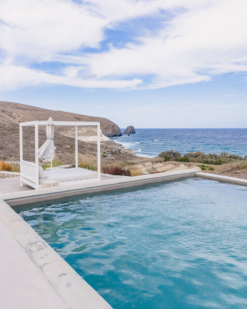 A corner of an infinity pool that faces the ocean, with a white canopy sunbed on the left of the pool.